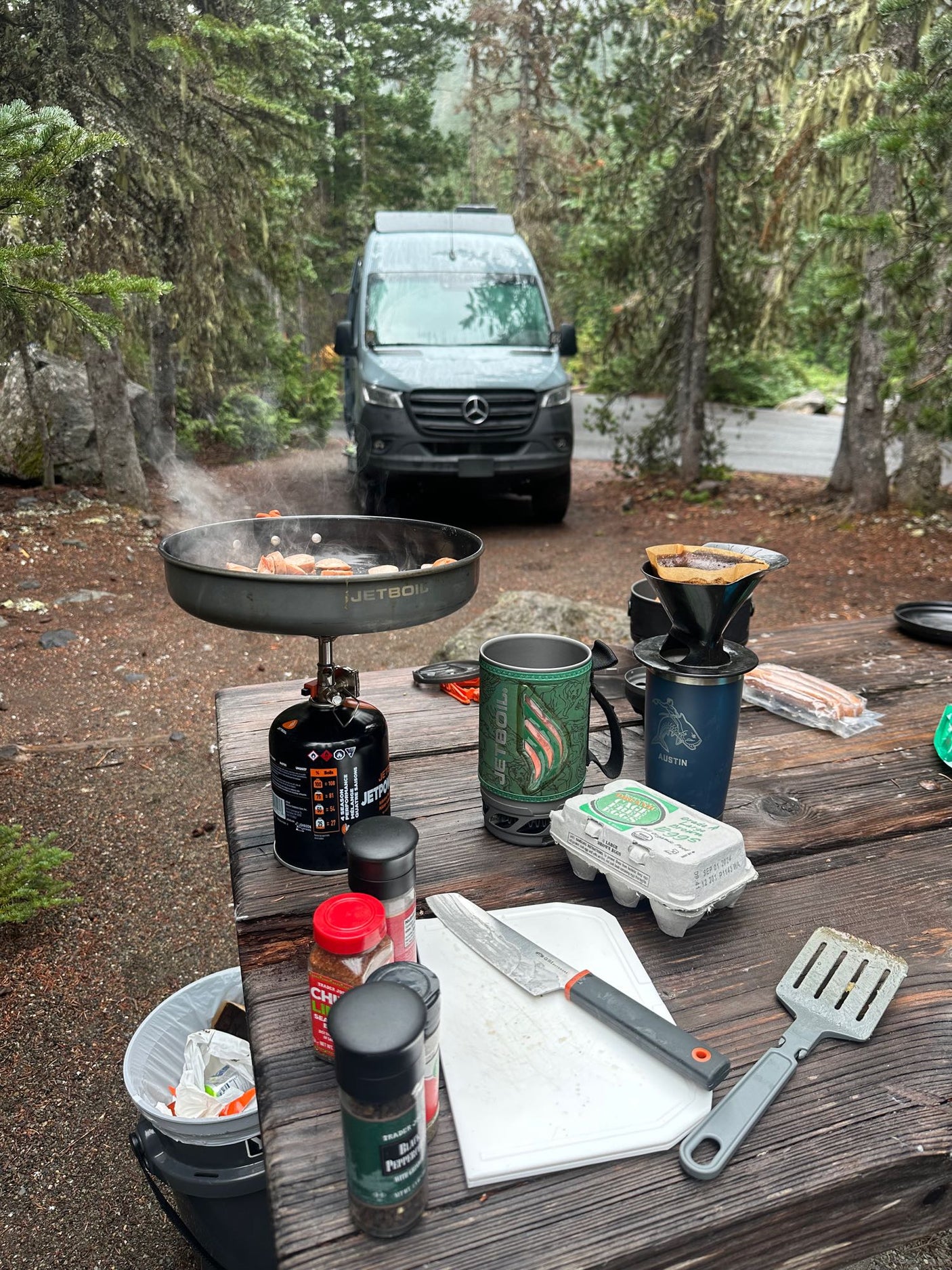 Campsite cooking next to an rv rental van. Breakfast with a Jetboil stove and coffee setup in nature.