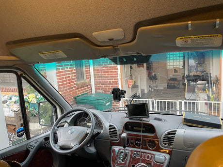 RV rental interior: Driver's view of the dashboard, steering wheel, and the exterior through the windshield towards a brick house.