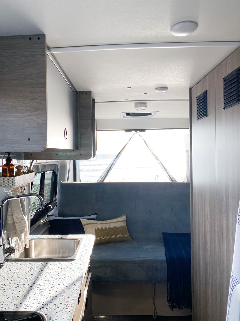 Cozy RV rental interior with a modern kitchenette, overhead storage, and comfortable bench seating facing a bright outdoor view. — photo 11