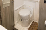 RV rental compact bathroom: white, modern toilet in a wet bath with a wooden slatted shower mat and light wood cabinetry.
