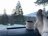 Cozy rv rental adventure: fuzzy socks, warm mug on dash, serene snowy mountains outside the window.