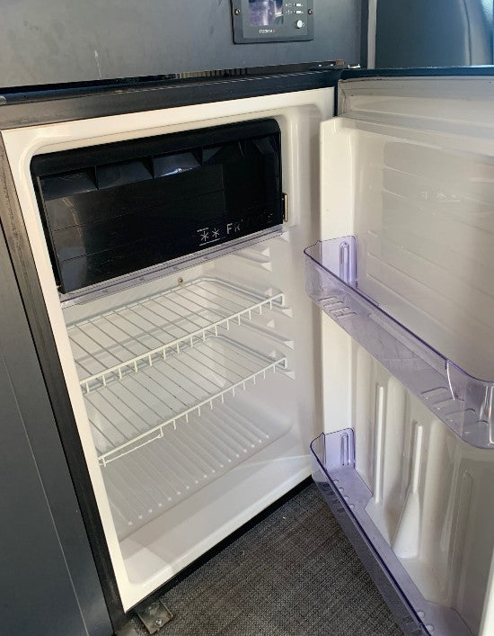 An open, clean RV rental mini-fridge showing its interior with wire shelves and a compact freezer compartment.