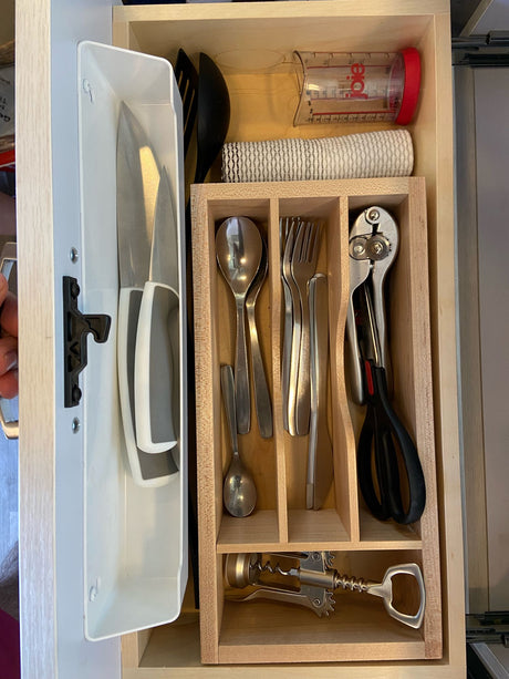Compact kitchen drawer organization for an RV rental. Knives, cutlery, measuring cup, and tools like a can opener are neatly stored.