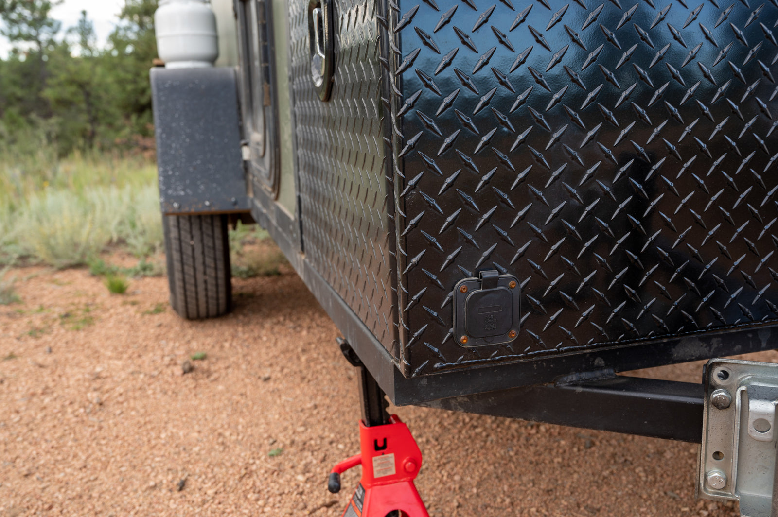 Close-up of a robust black diamond plate RV rental trailer, featuring a power inlet and red jack, for outdoor adventure.