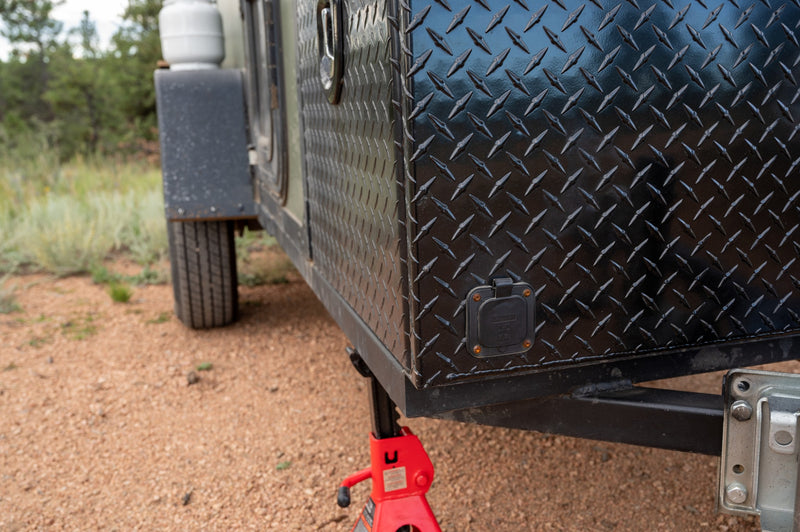 Close-up of a robust black diamond plate RV rental trailer, featuring a power inlet and red jack, for outdoor adventure. — photo 13