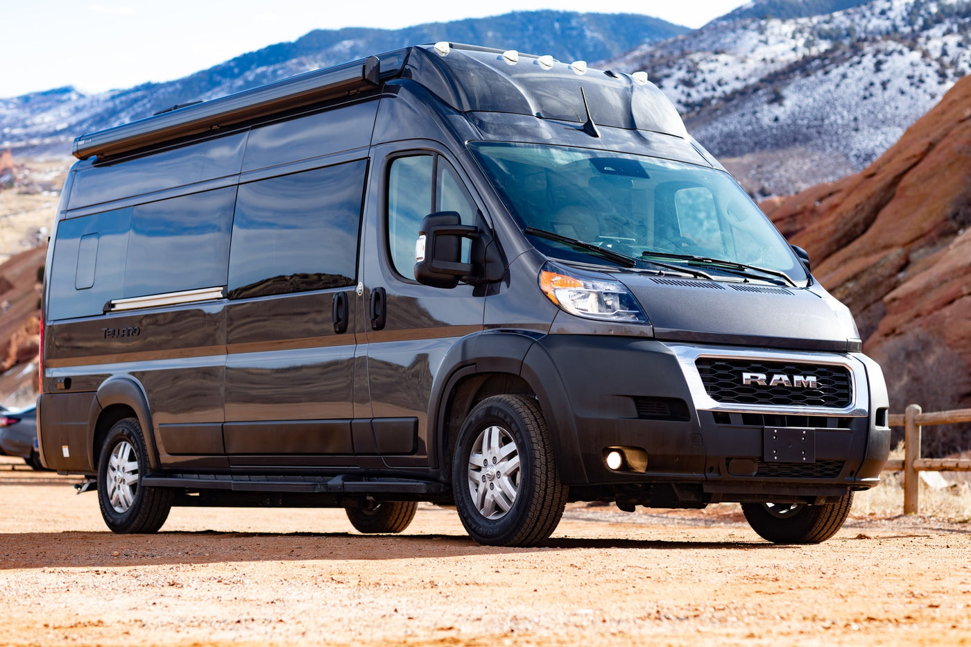  parked amidst scenic red rock formations.|Dark gray RV rental camper van on a dirt path. Snow-capped mountains and red rock formations create a scenic backdrop.|Dark gray RAM ProMaster camper van for rv rental parked on a dirt road — photo 9