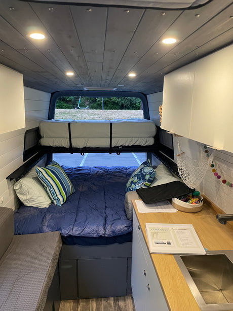 Interior view of an RV rental showcasing a cozy two-level bed system, kitchenette, and bright ceiling lights.