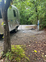 RV rental: A silver Airstream travel trailer hooked up at a tranquil, wooded campsite.