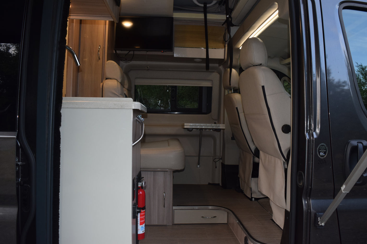 Interior of an rv rental from the open side door: shows a kitchenette, seating area with table, TV, and front driver seats.
