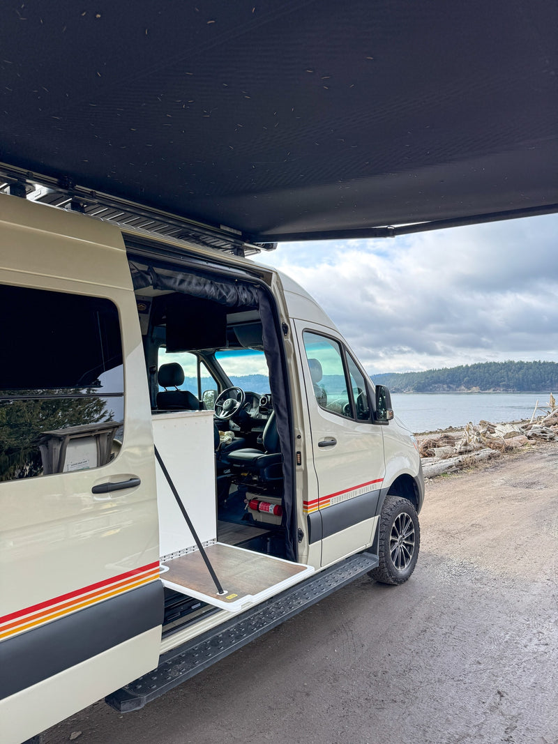 Beige Storyteller Overland camper van, door open with pull-out table, awning deployed by a scenic bay. Your ideal rv rental! — photo 10