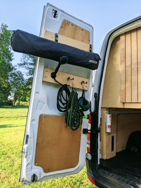 RV rental van rear door setup: Joolca outdoor shower, hoses, & storage, ideal for van life & camping adventures.