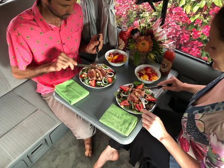 Couple dining on fresh salads & fruit in an rv rental, with vibrant flowers outside. A cozy travel meal.