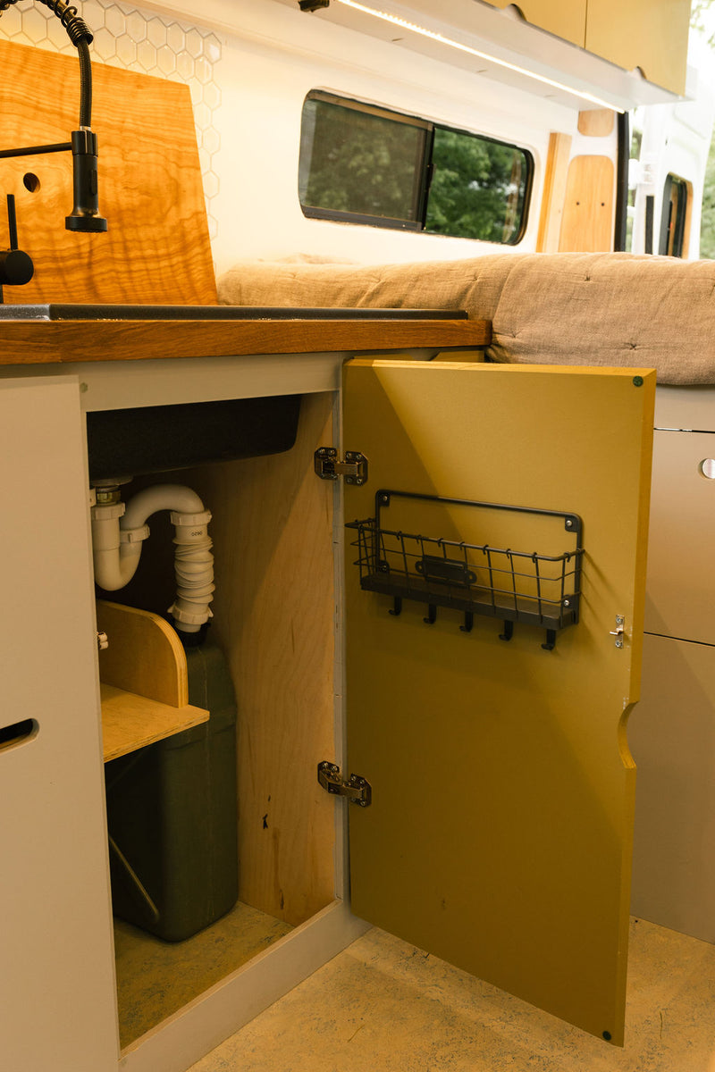 Compact RV rental kitchen with sink, under-cabinet plumbing, water tank, and door storage. — photo 12