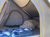 Cozy interior of a roof-top tent with blankets, pillows & storage net, perfect for your RV rental adventure.