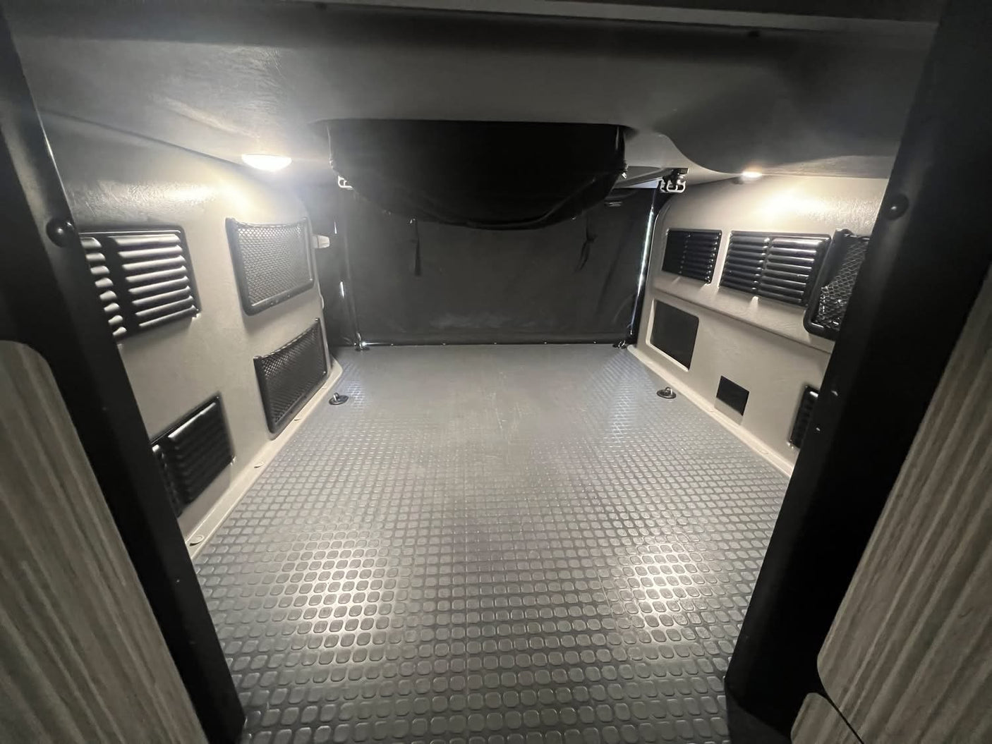 Spacious, empty RV rental interior with textured floor, wall vents, and bright overhead lighting, ready for your adventure.