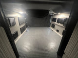Spacious, empty RV rental interior with textured floor, wall vents, and bright overhead lighting, ready for your adventure.