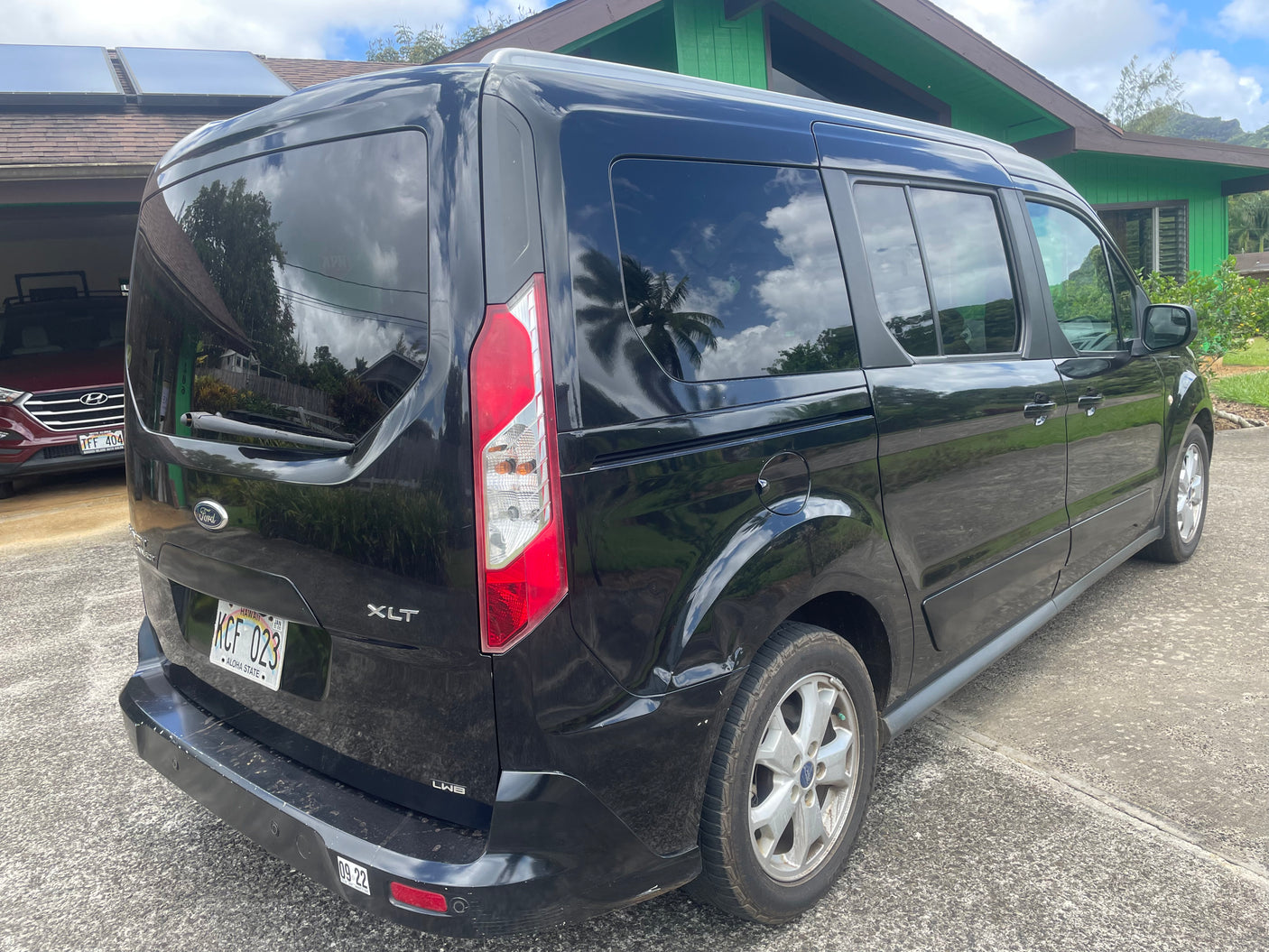 A black Ford Transit Connect XLT van, an adaptable vehicle ideal for adventure or an rv rental, parked on a sunny driveway.