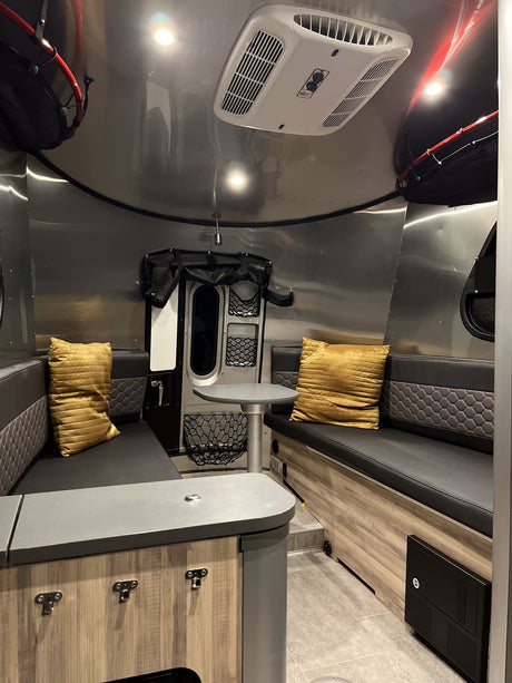 View inside a modern RV rental featuring metallic walls, black seating with yellow cushions, a table, and overhead AC.