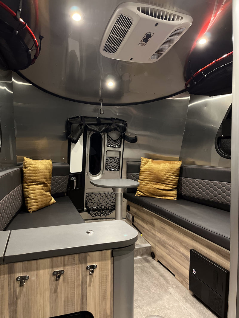 View inside a modern RV rental featuring metallic walls, black seating with yellow cushions, a table, and overhead AC. — photo 13