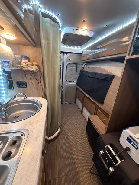 A cozy rv rental interior, showing a kitchenette with sink, overhead cabinets, and a portable power station on striped flooring.