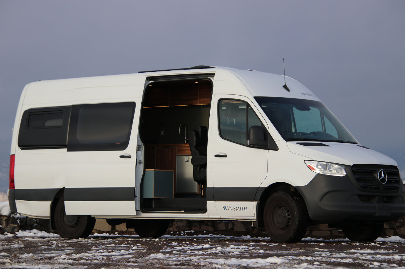 A white Mercedes-Benz Sprinter camper van, ideal for RV rental. Its open door reveals a custom, fully equipped interior for mobile living.
