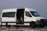 A white Mercedes-Benz Sprinter camper van, ideal for RV rental. Its open door reveals a custom, fully equipped interior for mobile living.