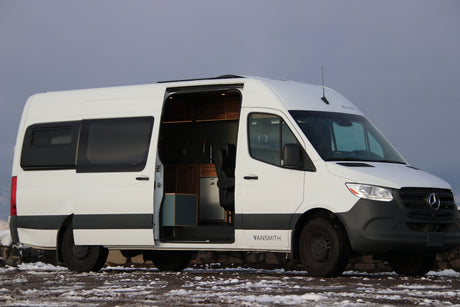 A white Mercedes-Benz Sprinter camper van, ideal for RV rental. Its open door reveals a custom, fully equipped interior for mobile living.