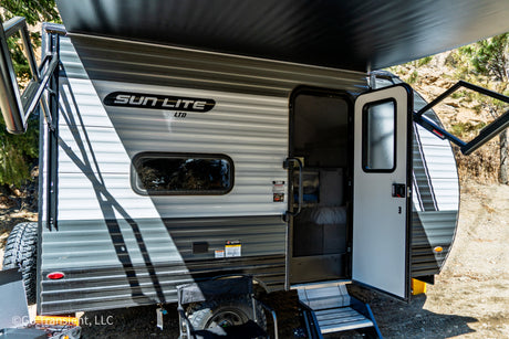 Sun Lite RV rental, a grey travel trailer, parked outdoors with awning extended and door open, ready for camping.