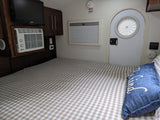 Cozy RV rental interior with a bed, checkered blanket, TV, AC unit, storage, window, and a unique round door.
