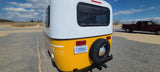 Rear view of a yellow & white P.O.P. Lite rv rental with a Michigan plate, parked by sand dunes.