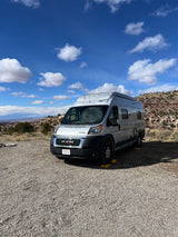 Silver Winnebago rv rental camper van leveled on gravel, with desert landscape and blue sky.
