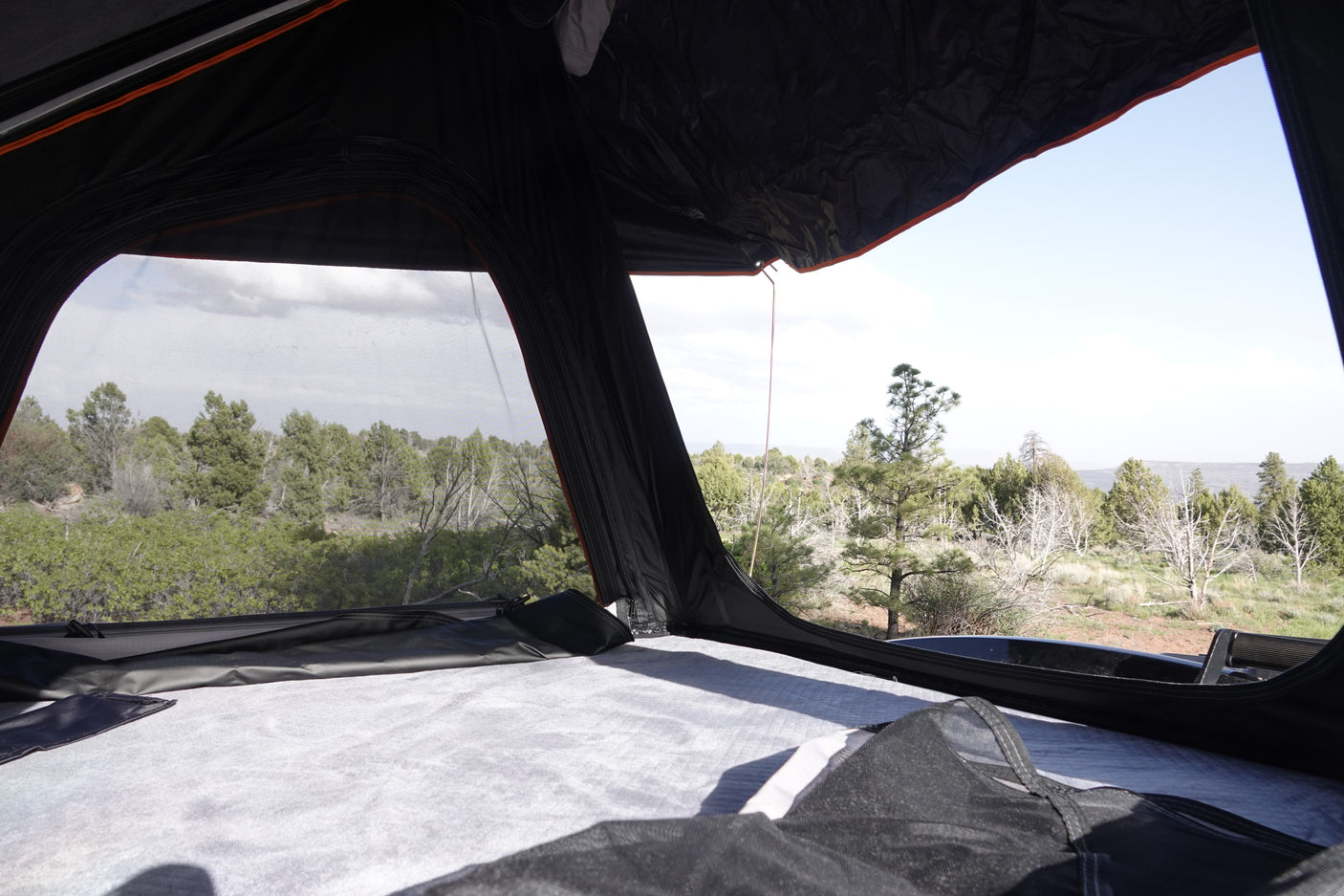 A cozy view from inside a black rooftop tent on an RV rental, overlooking trees and a distant landscape.