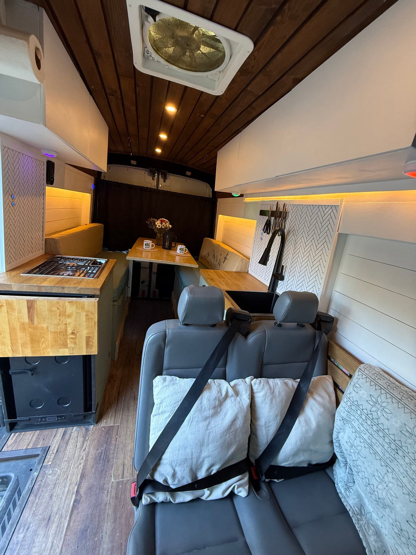 Well-appointed RV rental interior: kitchen with stove & sink, dining area, comfy rear seats, and wooden ceiling. Perfect for travel.