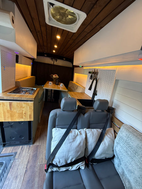Well-appointed RV rental interior: kitchen with stove & sink, dining area, comfy rear seats, and wooden ceiling. Perfect for travel.