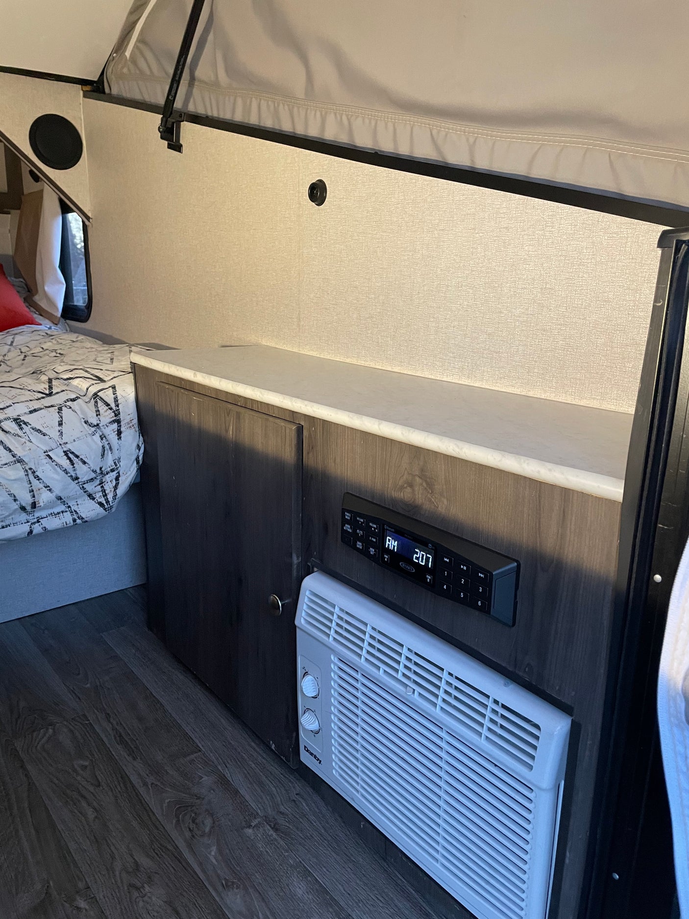 RV rental interior: compact sleeping area with bed, built-in counter, stereo, and air conditioner for comfort.