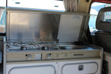 Interior view of a classic Westfalia camper van kitchen, with gas stove and sink, perfect for an RV rental.