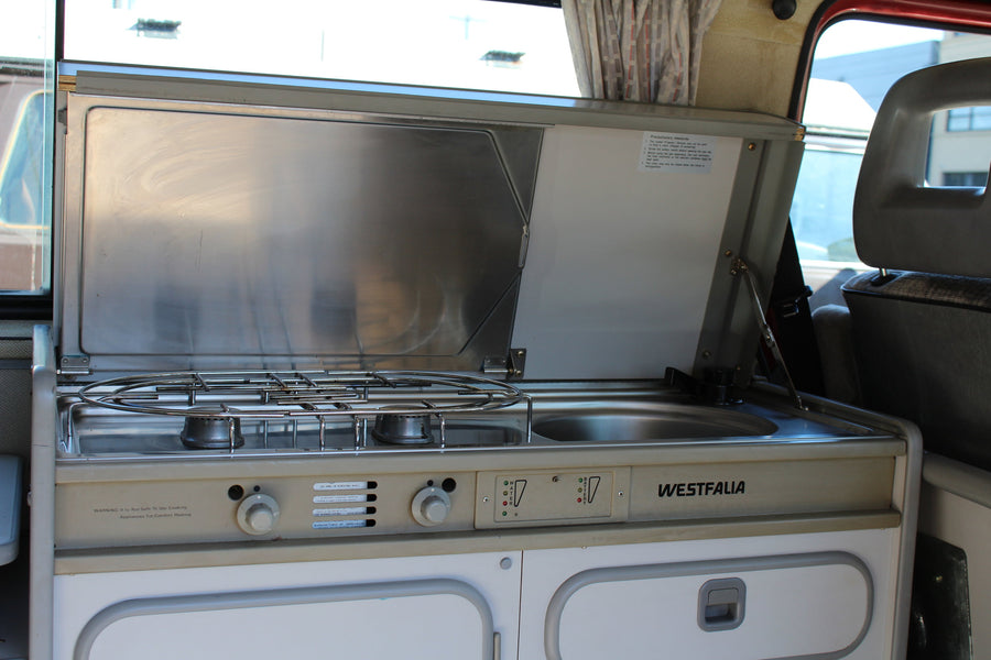 Interior view of a classic Westfalia camper van kitchen, with gas stove and sink, perfect for an RV rental.