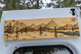 Woodburned mountain & forest art decorates an RV rental interior, showcasing trees and a blue river.