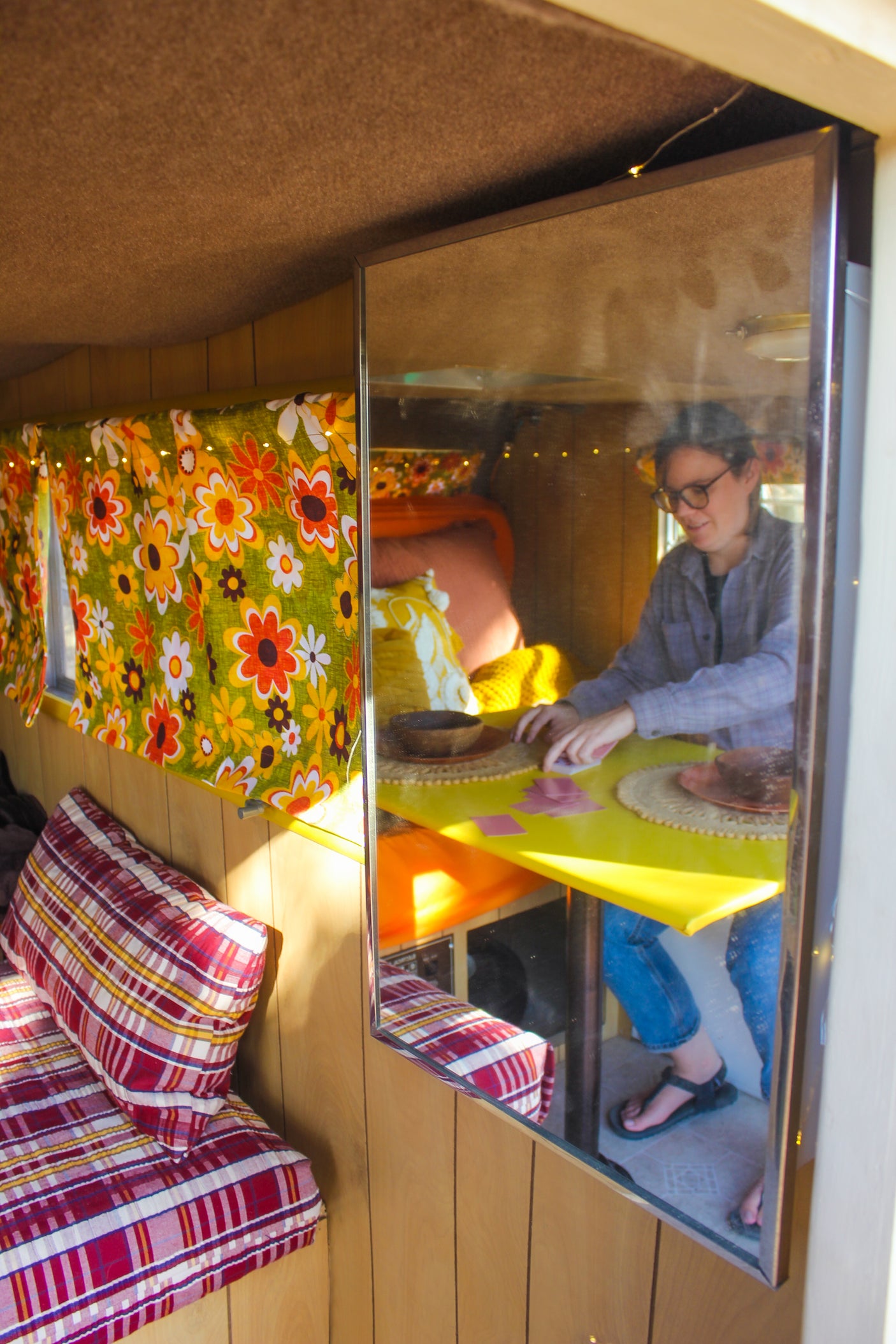 Inside this RV rental, a mirror reveals a person playing a game at a bright yellow table within a cozy, retro space.