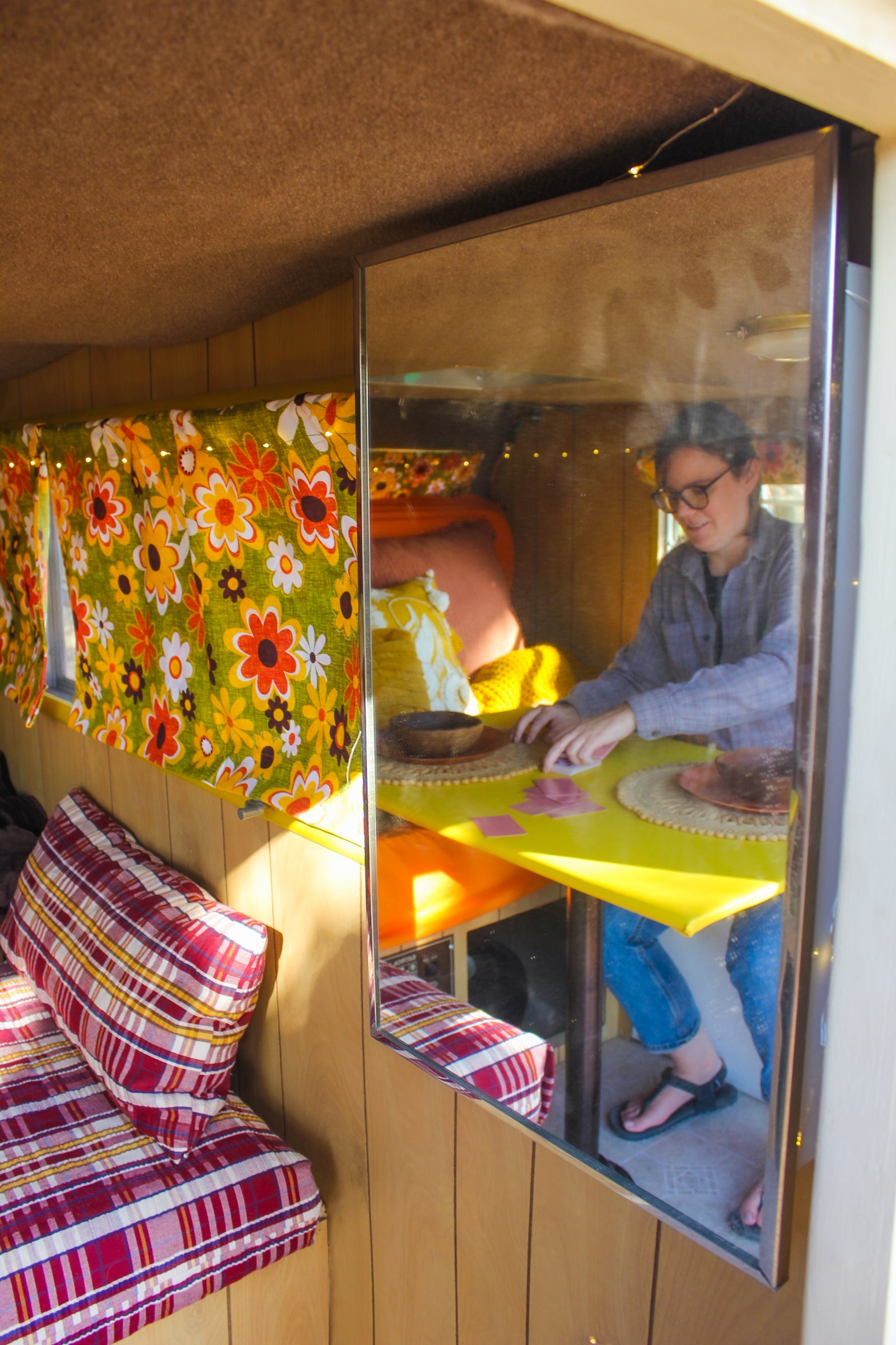 Inside this RV rental, a mirror reveals a person playing a game at a bright yellow table within a cozy, retro space.