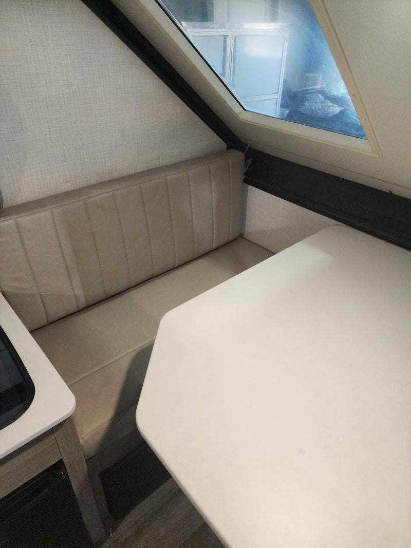 Bright RV rental dinette with comfortable bench seating, a white table, and an angled window, creating a functional camper interior. — photo 8