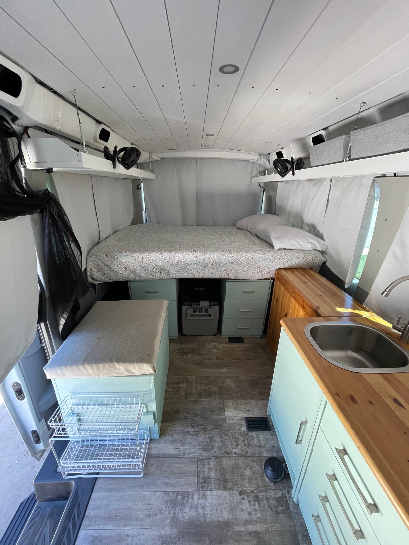Inside an RV rental: a modern camper van with bed, light blue kitchen, wood floors, and ample storage. — photo 5