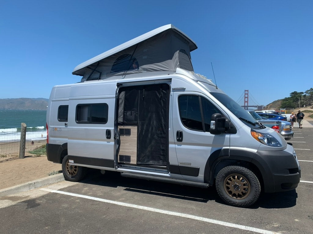 Silver Winnebago Solis RV rental parked by ocean with iconic Golden Gate Bridge views.