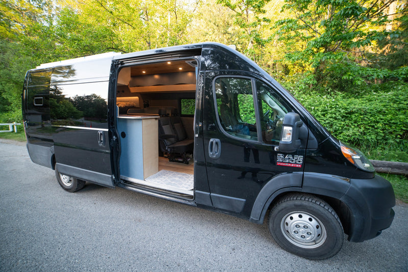 Sleek black RAM ProMaster camper van for rv rental. Open side reveals its custom wood interior with bed & seating. — photo 4