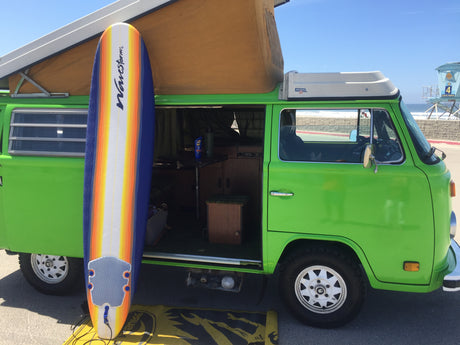 This bright green RV rental with its pop-top roof and a colorful surfboard is perfectly set for a beach adventure.