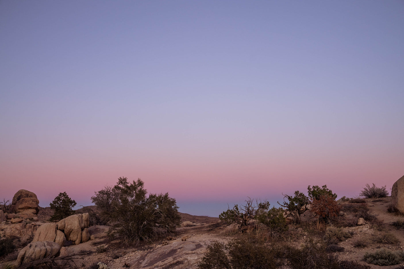 Experience tranquil desert beauty. A vibrant pink and lavender sunset over sparse rocks and brush. Ideal for an RV rental getaway.