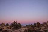 Experience tranquil desert beauty. A vibrant pink and lavender sunset over sparse rocks and brush. Ideal for an RV rental getaway.