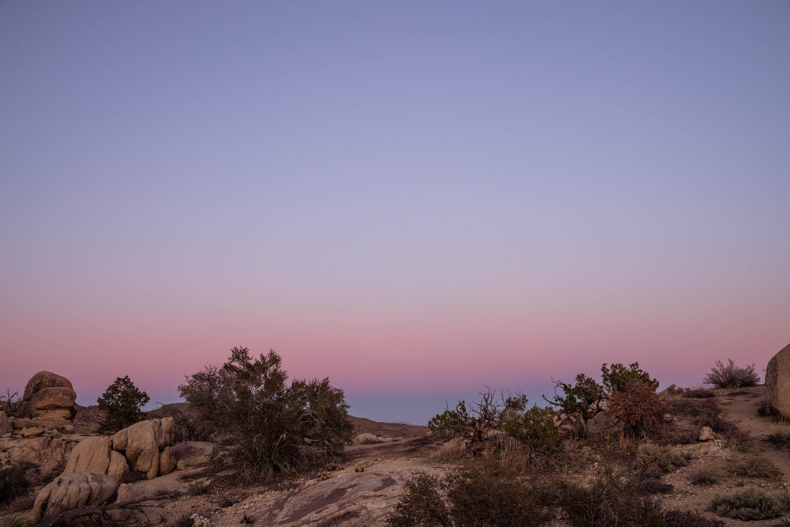 Experience tranquil desert beauty. A vibrant pink and lavender sunset over sparse rocks and brush. Ideal for an RV rental getaway.