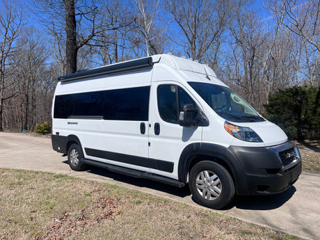 This white Thor Sequence campervan, perfect for an rv rental adventure, is parked on a sunny day with bare trees in the background.