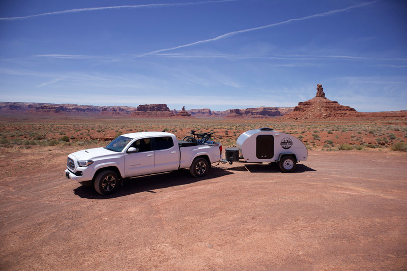White pickup truck with bikes and a teardrop RV rental camper parked in a vast red rock desert under a blue sky, ready for adventure. — photo 16